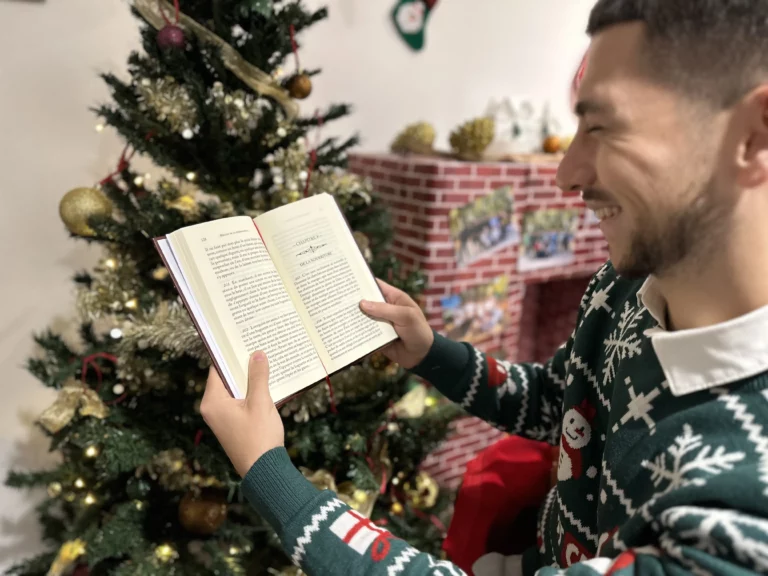 Homme lisant un livre devant un sapin de Noël, symbole de transmission et de moments conviviaux pendant les fêtes