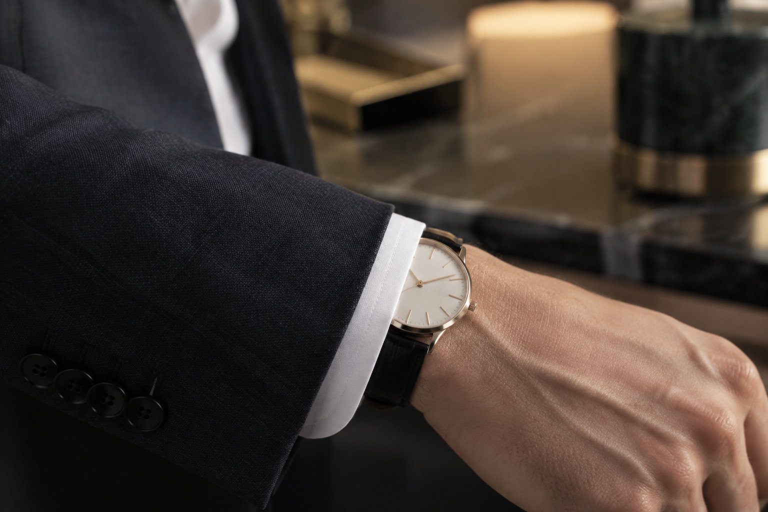 Un homme en costume regarde sa montre-bracelet dans un intérieur éclairé à la lumière chaude.